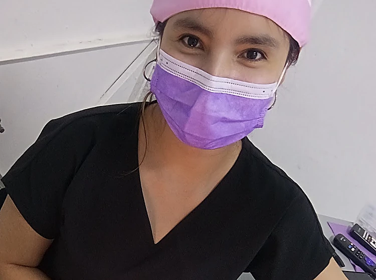 La doctora de Dentader con gorro rosa y cubrebocas lila en el consultorio