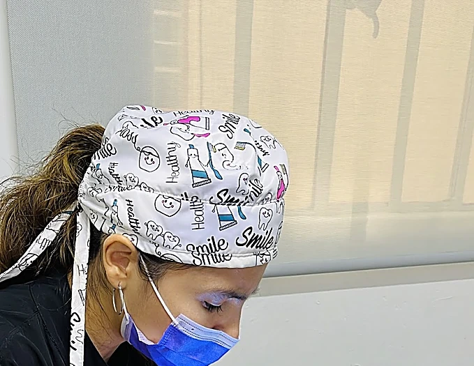 La doctora de Dentader con gorro quirúrgico estampado de dientes y cubrebocas, atendiendo en el sillón